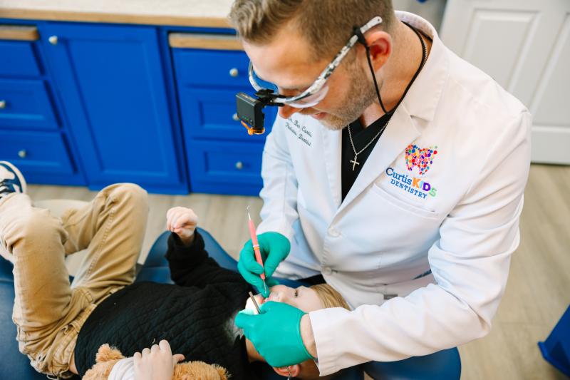 Dentist performs pediatric tooth extraction in clean, modern office.